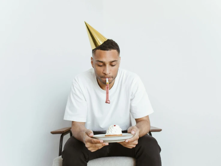 a man sitting on a chair wearing a party hat while eating cake