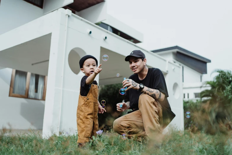 two boys blowing soap bubbles while sitting in the grass