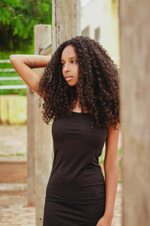 a girl wearing a black dress, leaning on a wooden post