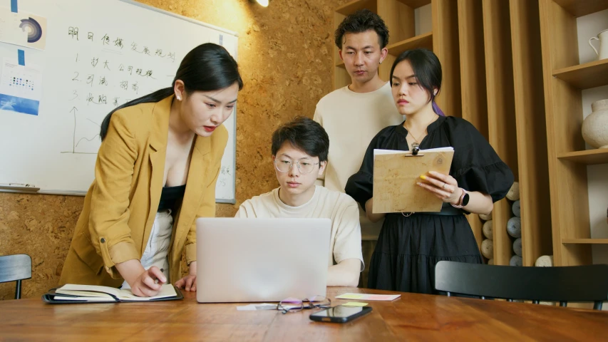 a woman is working on a laptop with other people looking at it