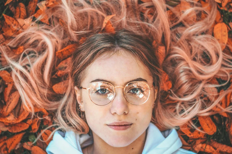 a young woman with glasses wearing glasses laying in leaves