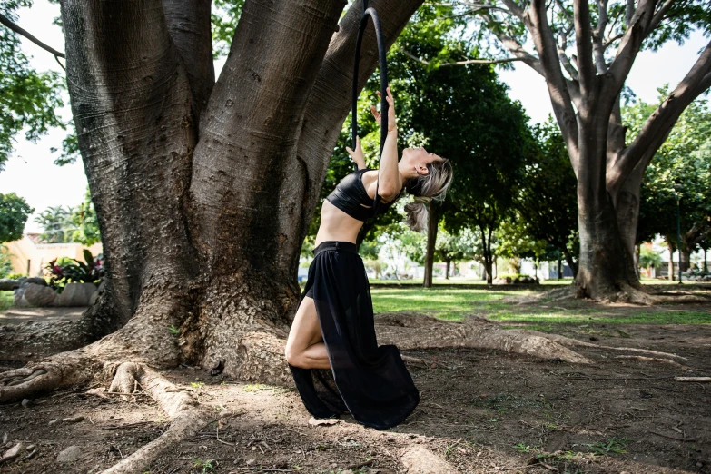 a young woman in a black outfit leans up against a tree