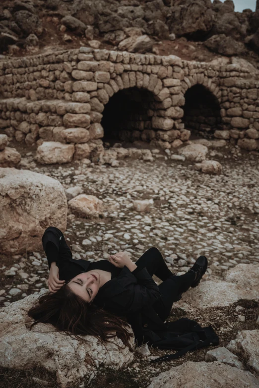 a woman laying on a rocky cliff with her head resting on her legs