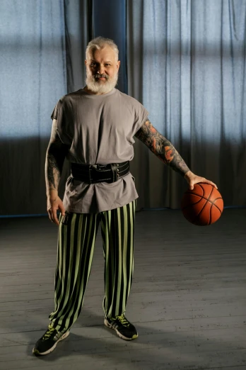 a bald man in striped pants holding a basketball