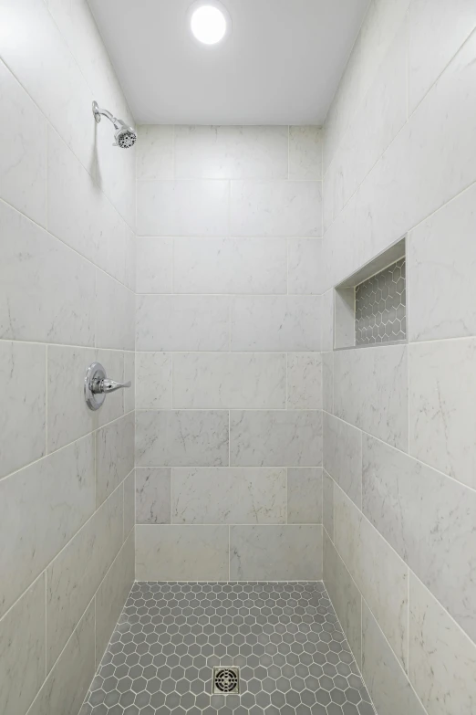 a white tiled bathroom with a drain sitting in the middle