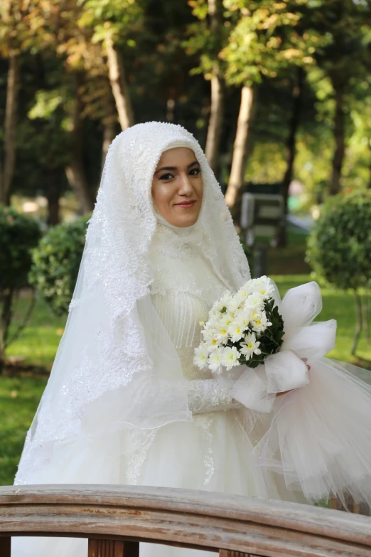 a woman in a dress and veil holding flowers on a bench