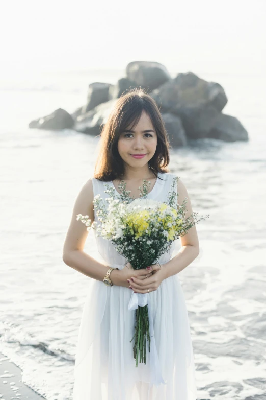 woman standing on beach holding flowers in front of water