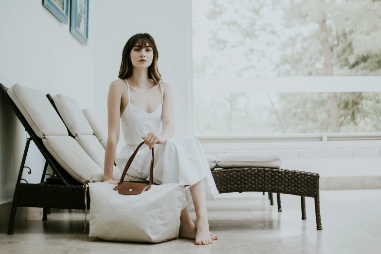 the girl is sitting on a chair holding a white bag