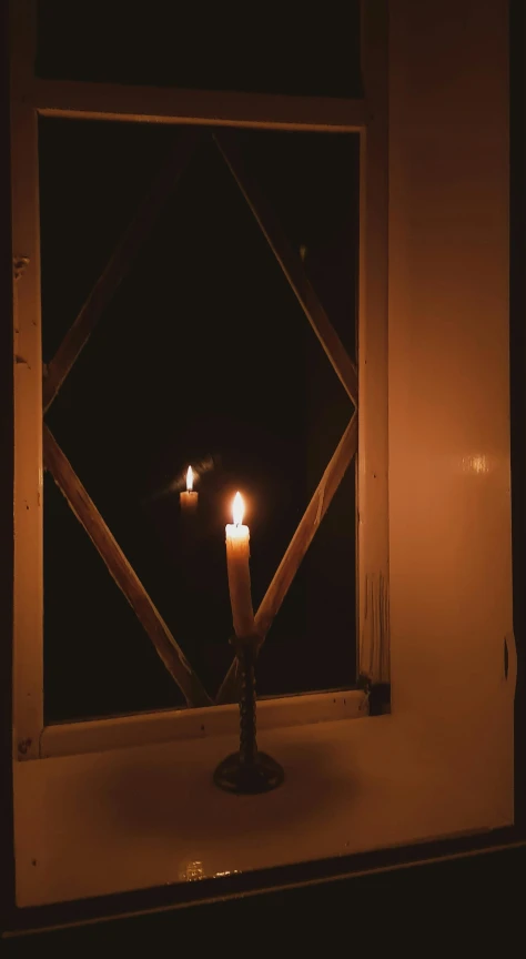 a single candle sitting on a windowsill with a dark background