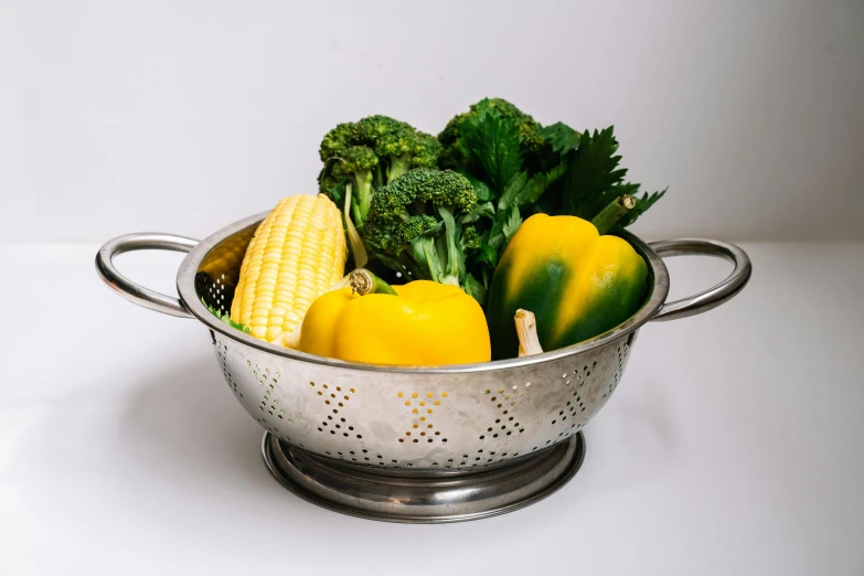 a metal colander holding vegetables and corn