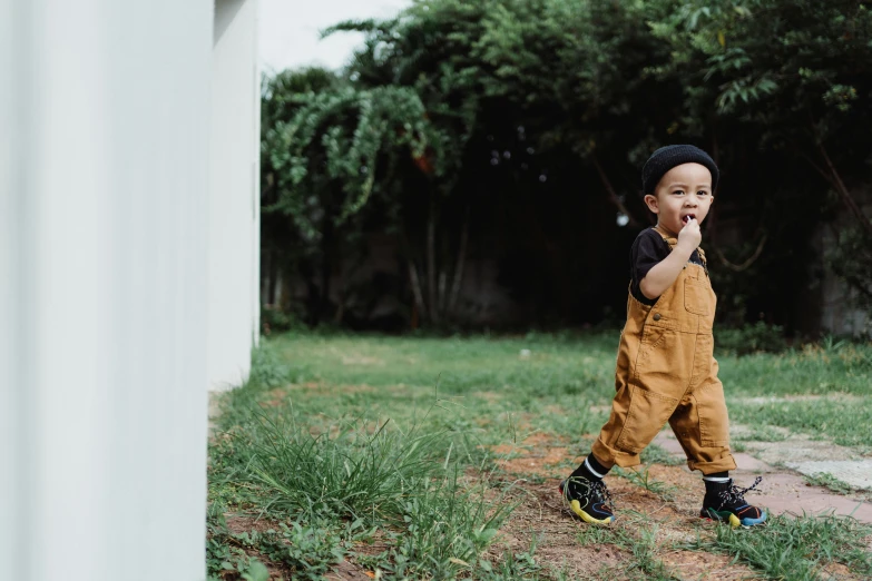 a little boy standing in the grass wearing a black hat