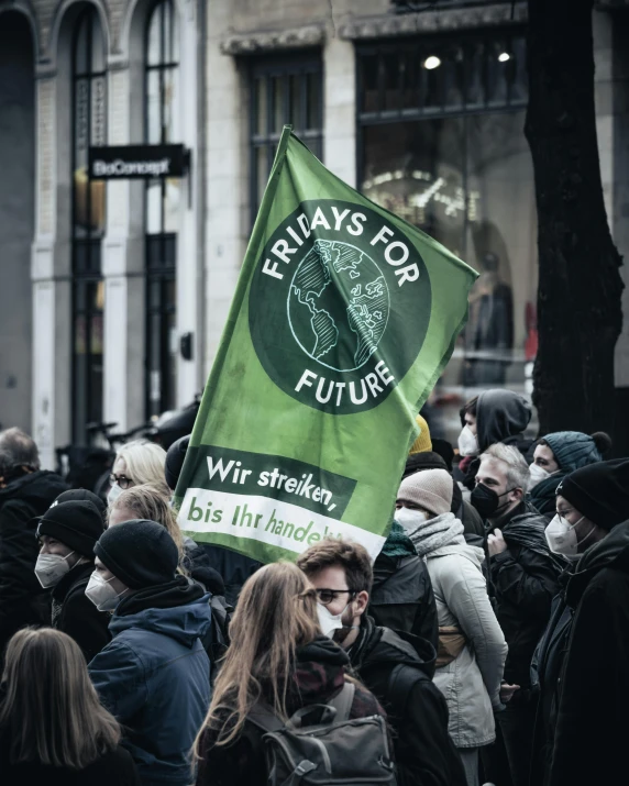 a protest with a green flag and a black banner that reads fridays for future