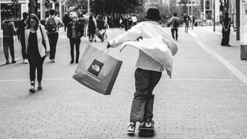 black and white po of boy on skateboard carrying bags