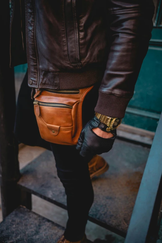 a man with a black jacket and jeans holding a leather bag