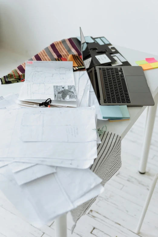 stacks of papers and a laptop are on a table