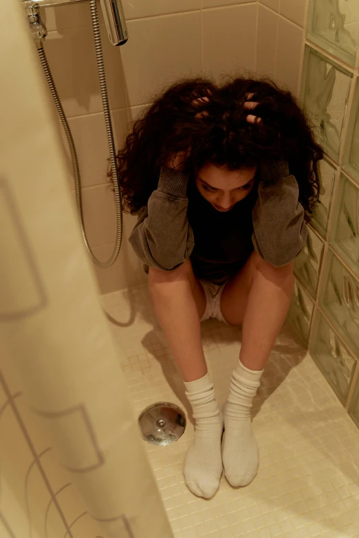 a woman sitting in a bathroom next to a shower with her legs crossed