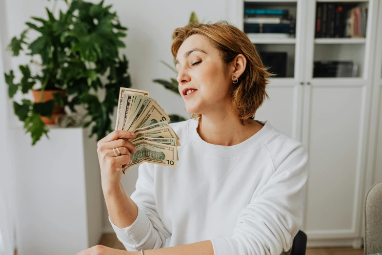 the woman is sitting in front of the computer holding her money