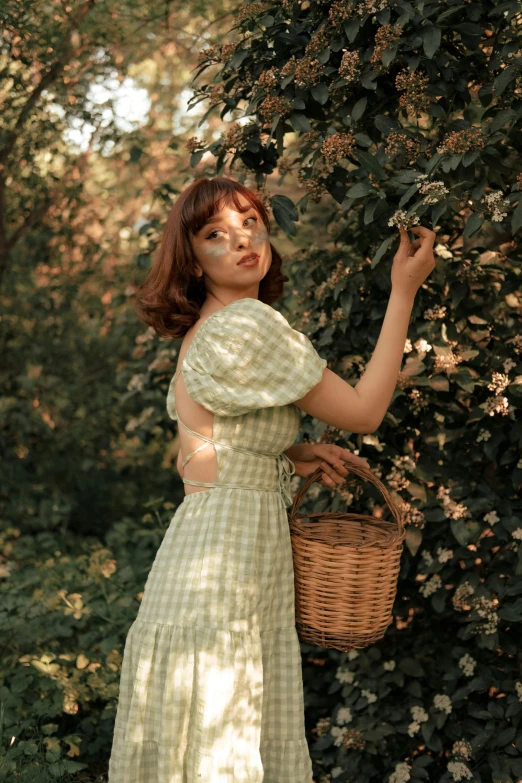 a young lady with long brown hair is holding a basket while wearing a green dress