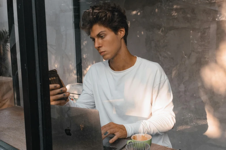 a boy is sitting at a table using his laptop