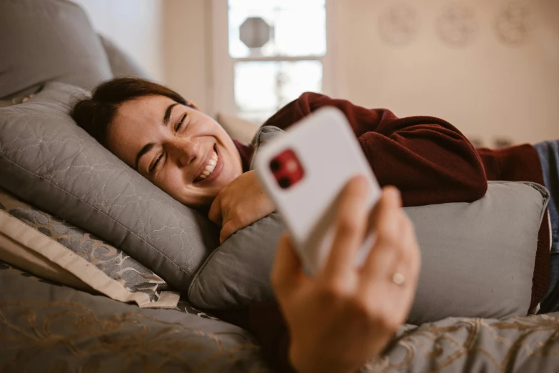 a smiling girl lying down on the bed, holding a remote control in her hand