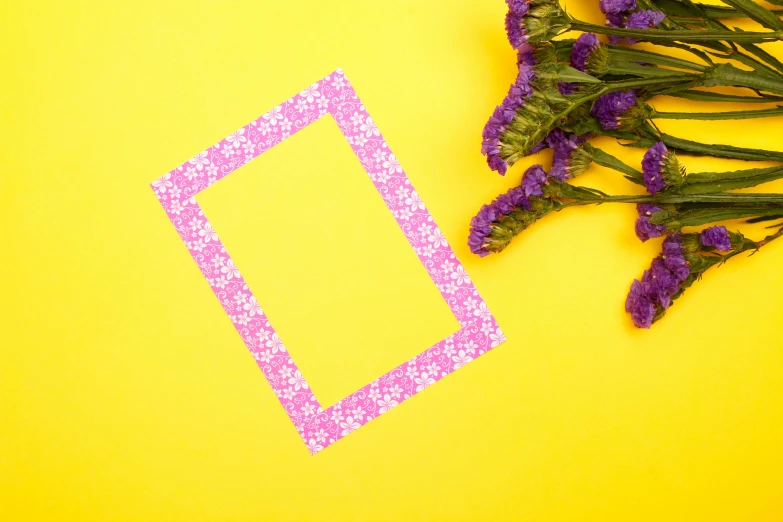 purple flowers are on a yellow surface near a pink frame