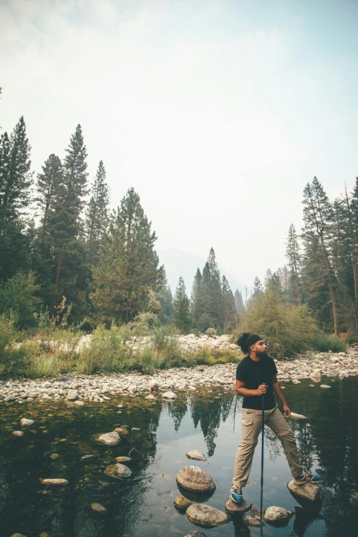 man standing on rock stepping on small stream in wooded area