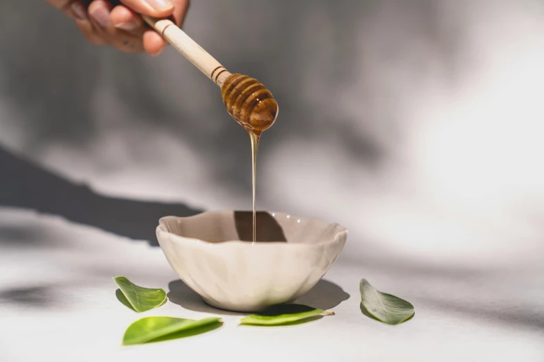 a hand drizzling honey onto a white bowl