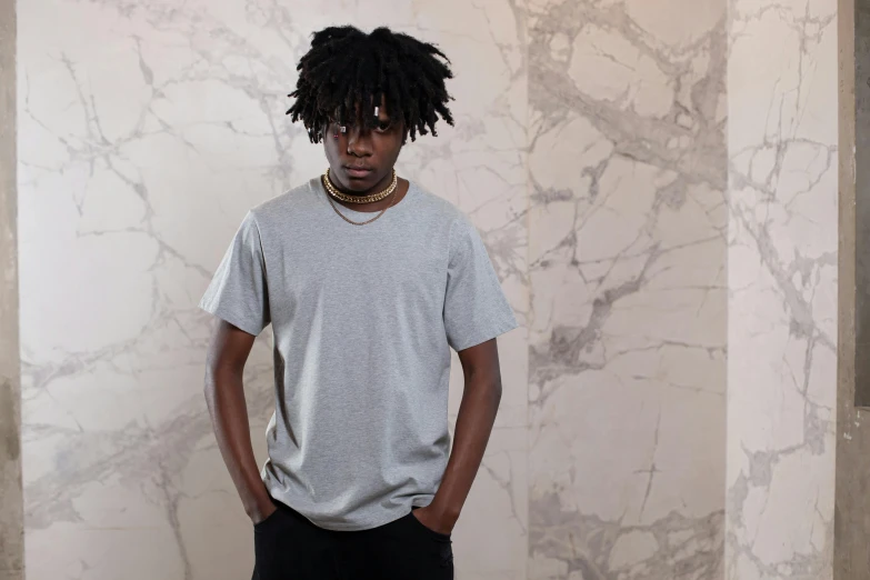 a young man stands in a white room wearing a grey shirt