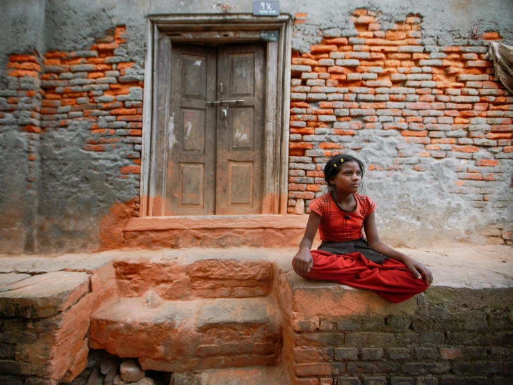 an indian girl sits alone outside of her house