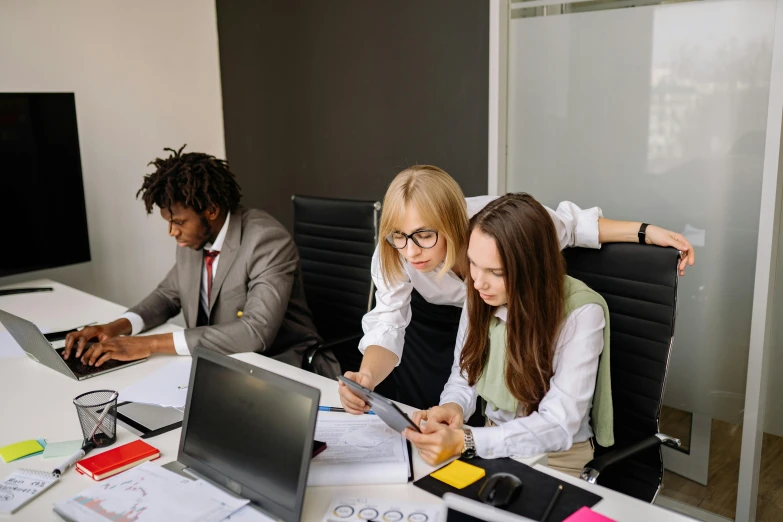 three young women at a desk using laptops and phone