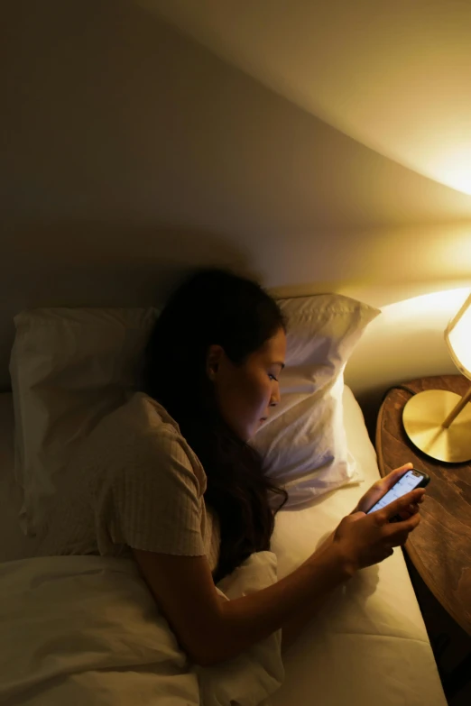 a woman laying in bed while using a cell phone