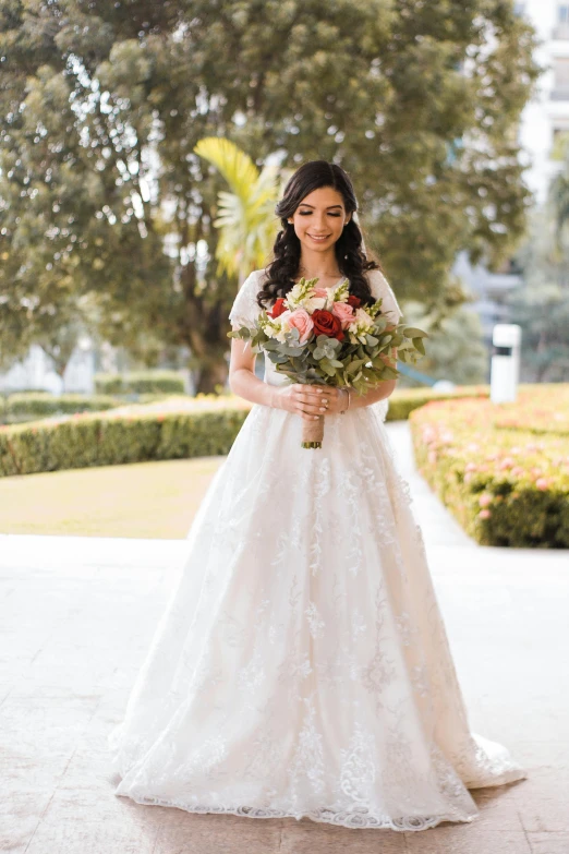 a woman holding flowers stands outside in her wedding gown