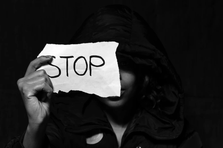 a woman wearing a hoodie and a piece of paper that reads stop in black and white