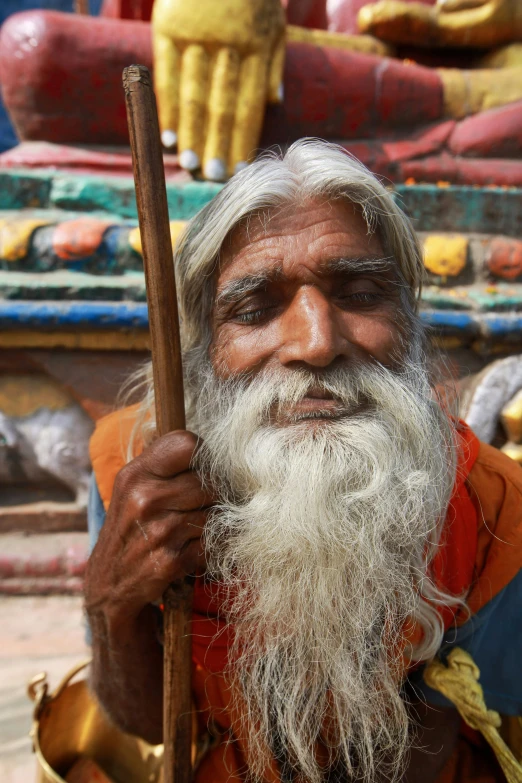 the man is holding a stick standing by an outside sculpture