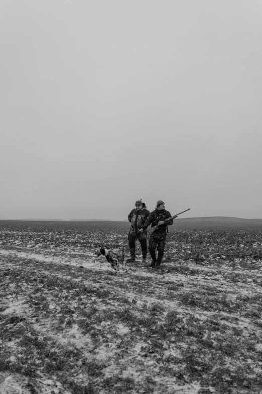 two men walking across a snow covered field with an old rifle in hand