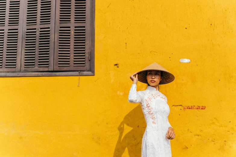 a woman with a big hat is standing in front of a yellow building