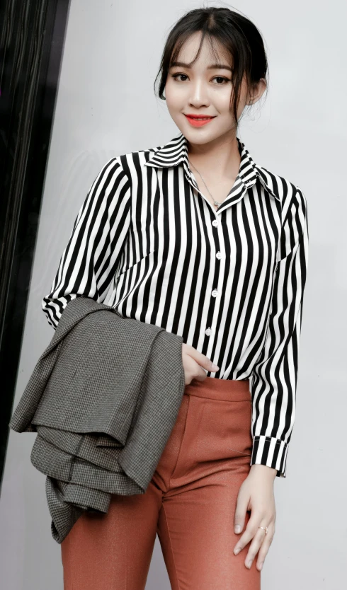 a woman standing in front of a wall, wearing a striped shirt and pants