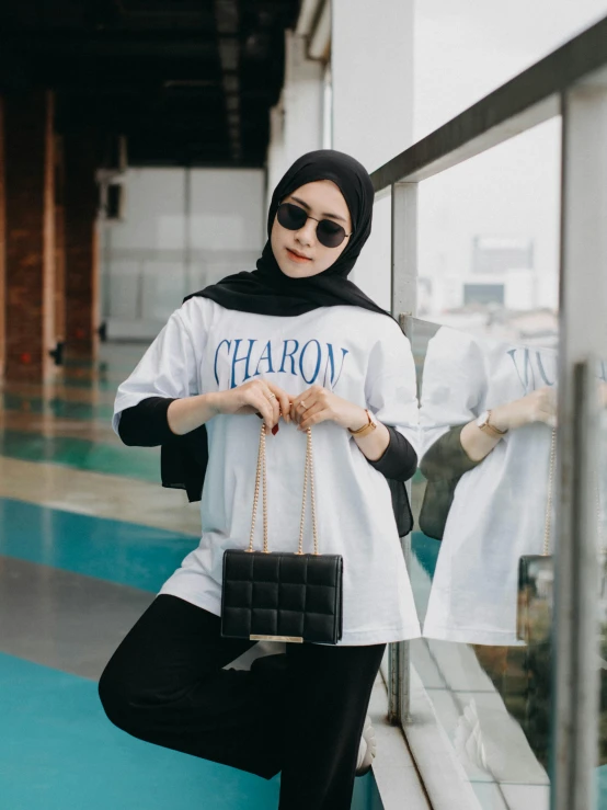 a woman in hijab, shirt and pants standing by the window