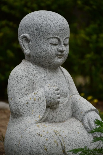 a stone statue sits in the grass near flowers