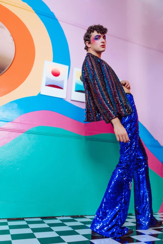 a young man standing against a wall with a colorful pattern