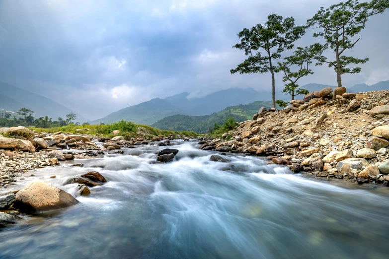 small stream running past rocky hillside under a cloudy sky