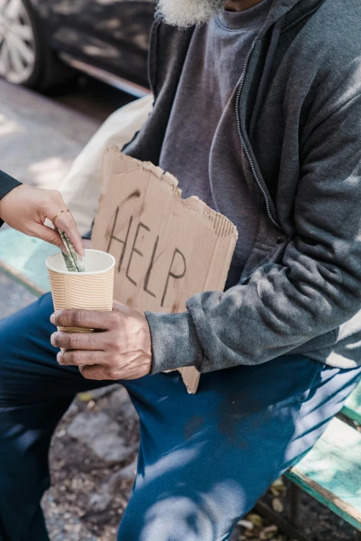 an elderly man holding a cup and a cardboard sign reading help