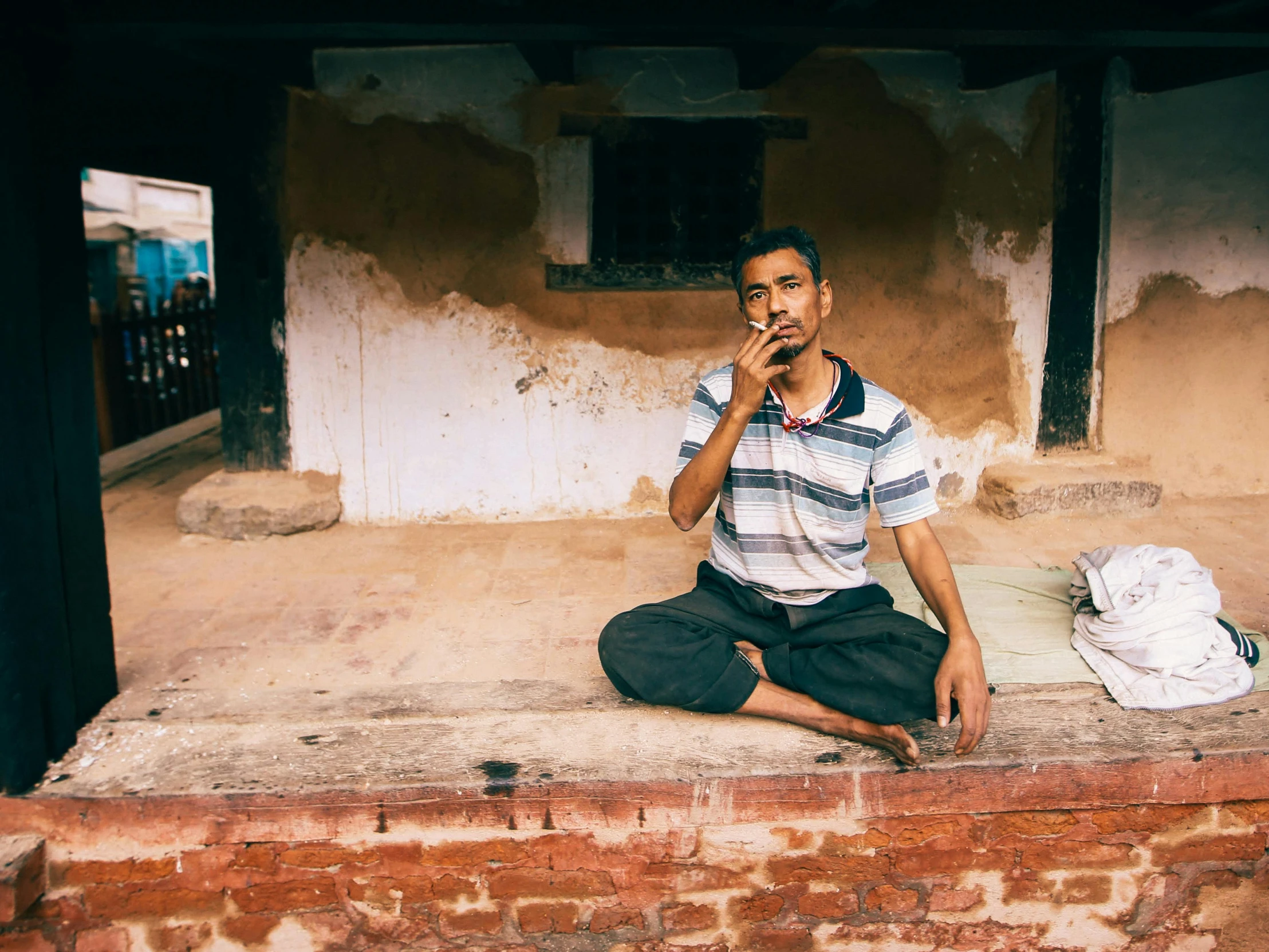 a man sitting on the ground next to a building smoking