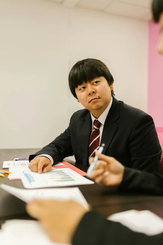 an asian man is discussing his work while seated at the table