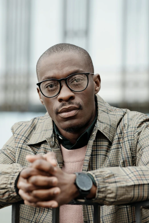 a man wearing glasses looks pensive while leaning against a railing