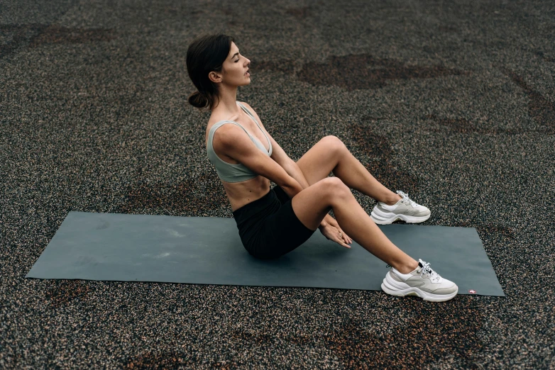 a woman sitting on her stomach, tying with a gym mat