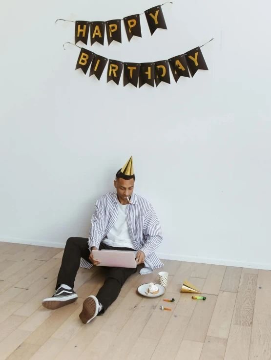 a man wearing a birthday hat sits next to a birthday cake