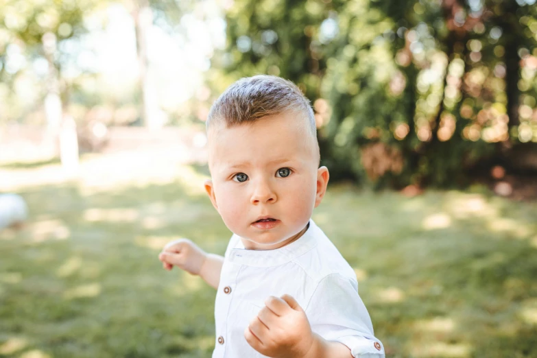 a little boy with a shaved head standing in the grass