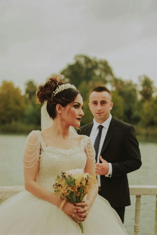 the newly couple is standing on the bridge near a body of water