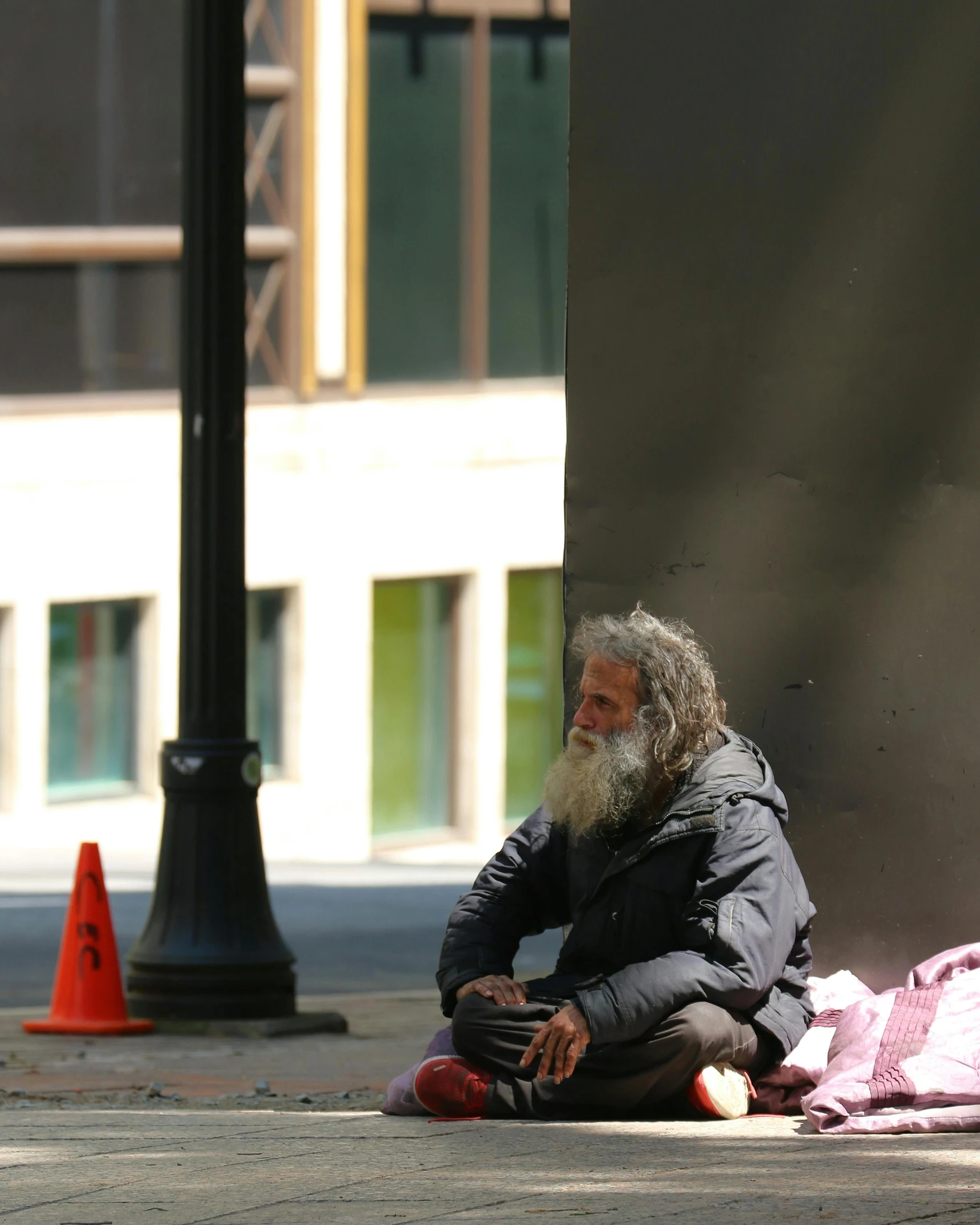 man with long beard sitting on sidewalk next to traffic cone